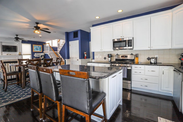 kitchen with ceiling fan, a center island, dark stone countertops, white cabinets, and appliances with stainless steel finishes