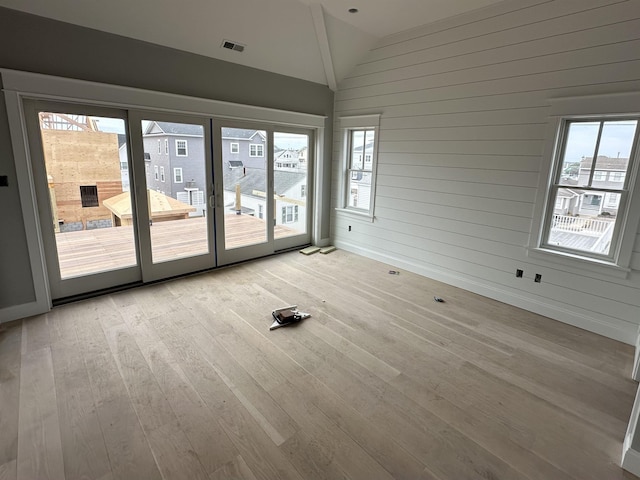 unfurnished room with vaulted ceiling, wood walls, and light hardwood / wood-style flooring