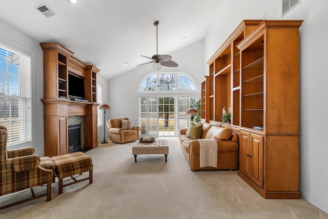 living area with light carpet, ceiling fan, visible vents, and a glass covered fireplace