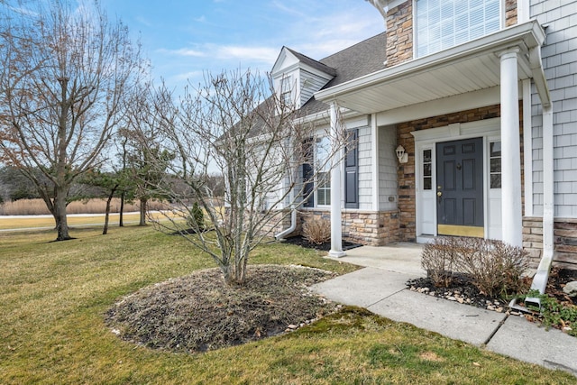 doorway to property with stone siding, a lawn, and roof with shingles