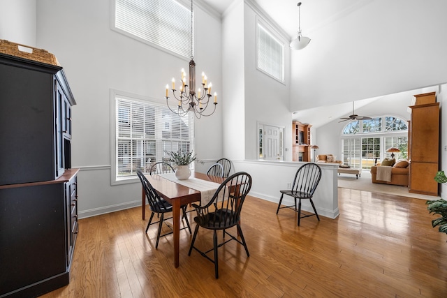 dining area featuring light wood-type flooring, a towering ceiling, baseboards, and ceiling fan with notable chandelier