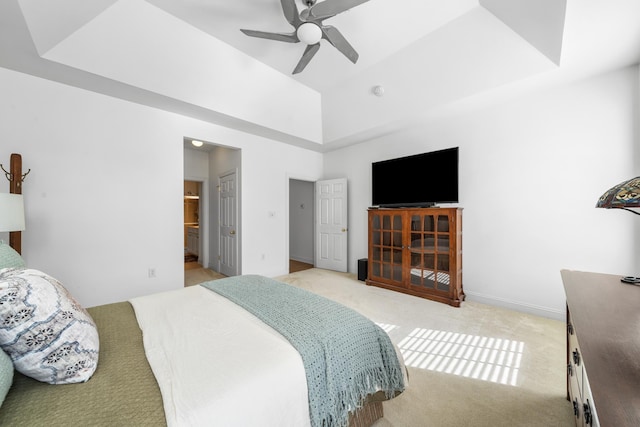 bedroom with light carpet, baseboards, a raised ceiling, ceiling fan, and ensuite bath