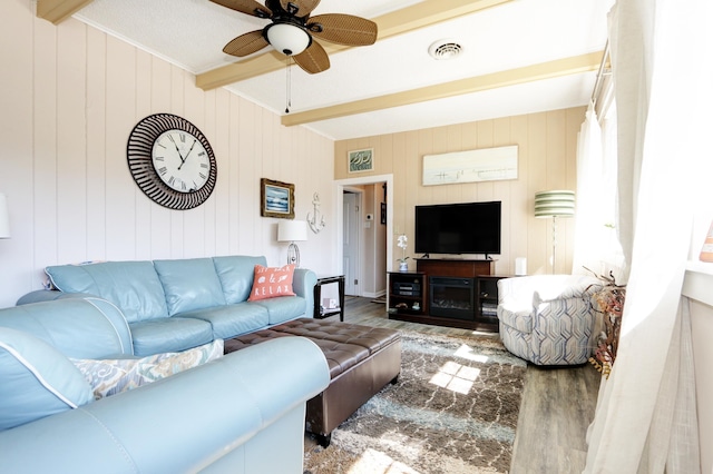 living room with ceiling fan, wooden walls, beamed ceiling, and hardwood / wood-style flooring