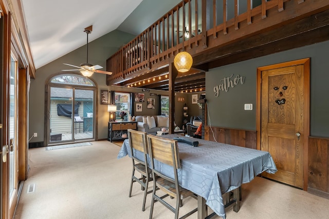 carpeted dining space with wood walls, ceiling fan, and lofted ceiling