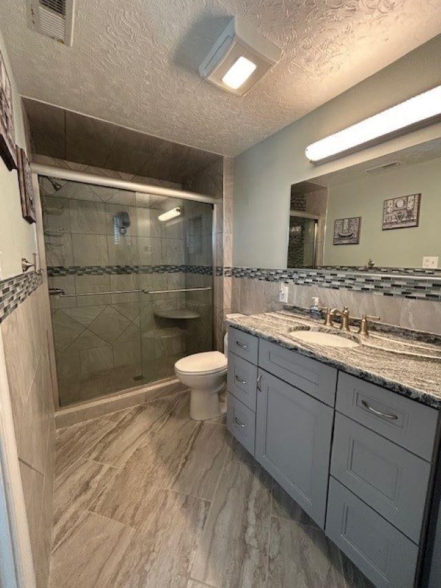 full bathroom featuring a stall shower, toilet, tile walls, and a textured ceiling