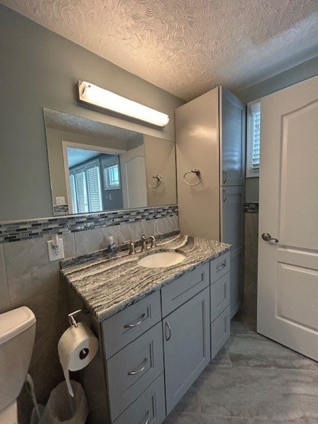 bathroom featuring toilet, a textured ceiling, vanity, and tile walls