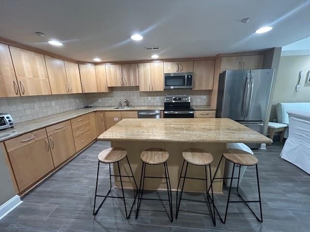 kitchen featuring a breakfast bar area, stainless steel appliances, decorative backsplash, and light brown cabinetry