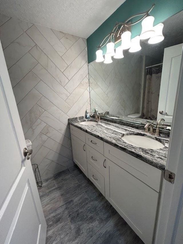 bathroom with double vanity, a textured ceiling, tile walls, and a sink