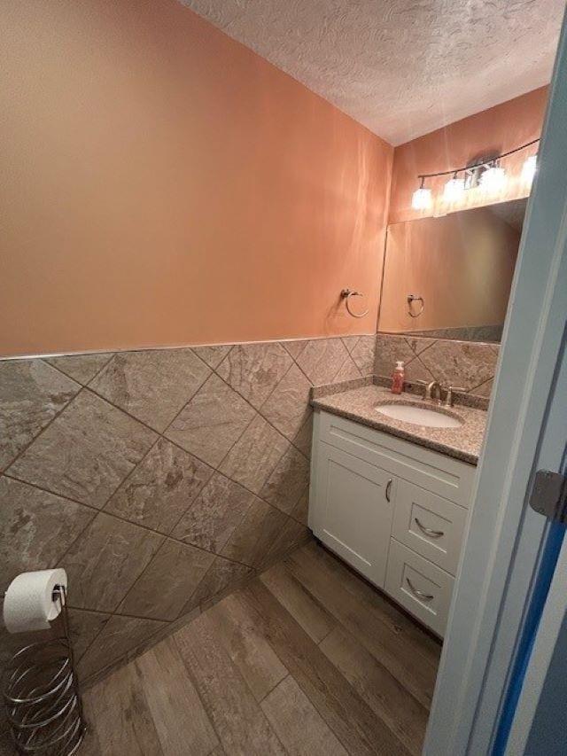 bathroom featuring a textured ceiling, a wainscoted wall, wood finished floors, vanity, and tile walls