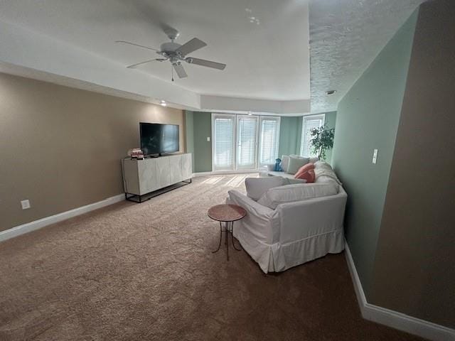 living area with a textured ceiling, carpet flooring, a ceiling fan, baseboards, and a raised ceiling