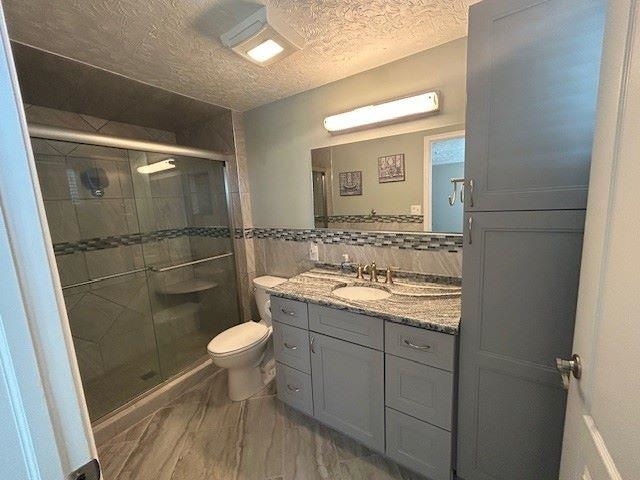 bathroom with toilet, a shower stall, tile walls, and a textured ceiling