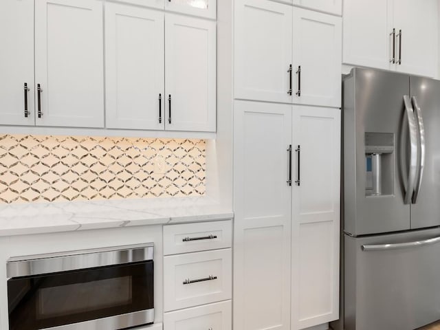 kitchen featuring tasteful backsplash, white cabinetry, appliances with stainless steel finishes, and light stone counters