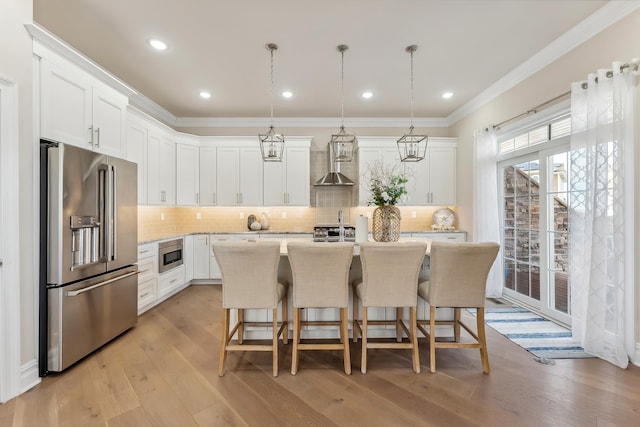 kitchen with crown molding, wall chimney range hood, light wood-type flooring, appliances with stainless steel finishes, and white cabinetry