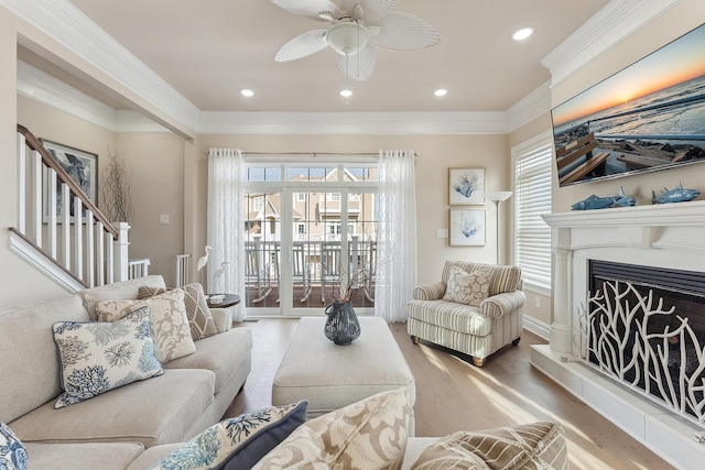 living area with plenty of natural light, a fireplace with raised hearth, crown molding, and wood finished floors