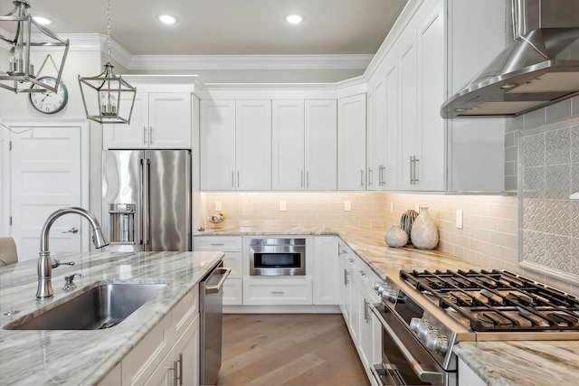 kitchen with a sink, stainless steel appliances, white cabinets, crown molding, and wall chimney range hood