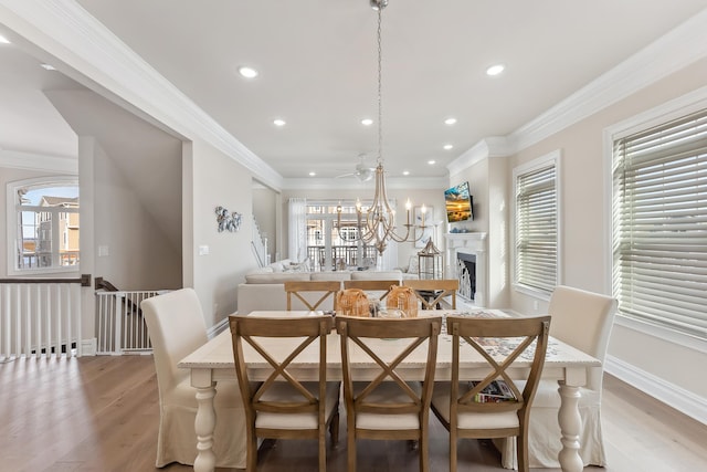 dining space featuring a fireplace, light wood-type flooring, an inviting chandelier, and ornamental molding