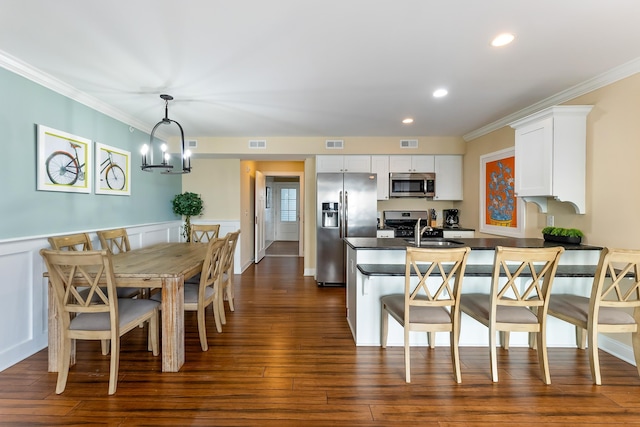 kitchen featuring pendant lighting, a breakfast bar, appliances with stainless steel finishes, white cabinetry, and dark hardwood / wood-style flooring