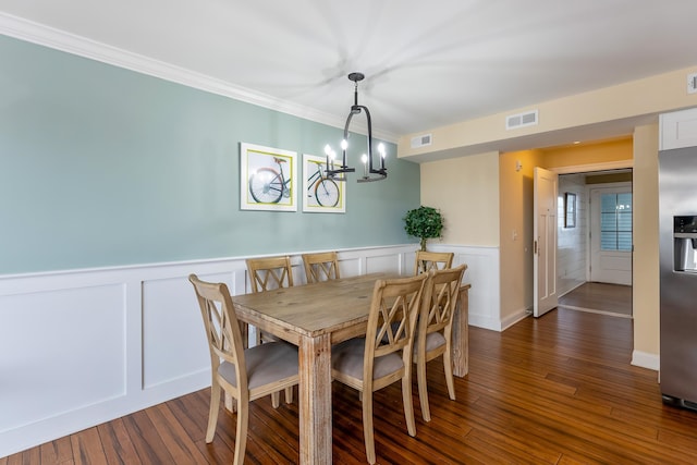 dining space with crown molding, dark wood-type flooring, and an inviting chandelier