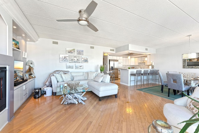 living room with light wood finished floors, a fireplace, visible vents, and a ceiling fan