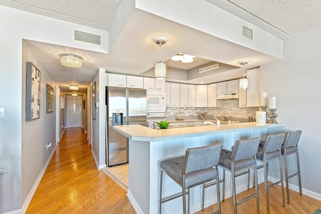 kitchen with a peninsula, white microwave, visible vents, and stainless steel refrigerator with ice dispenser