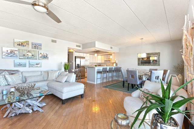 living room featuring light wood-type flooring, visible vents, and ceiling fan