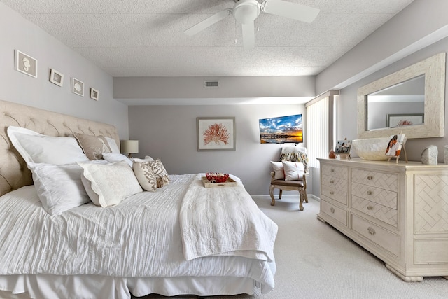 bedroom featuring a textured ceiling, light colored carpet, a ceiling fan, baseboards, and visible vents