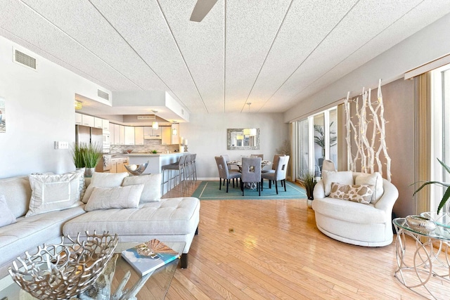 living area with light wood finished floors, baseboards, visible vents, and a ceiling fan