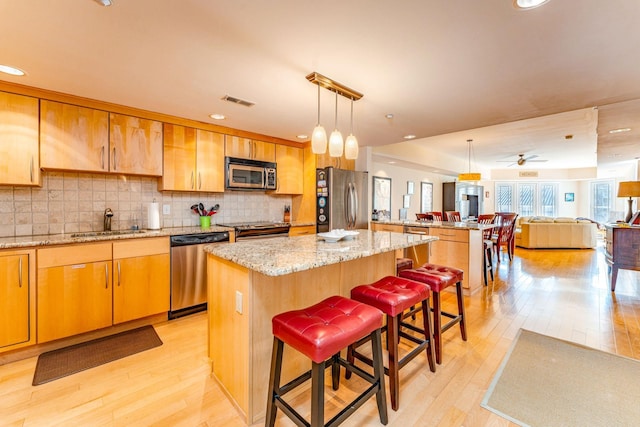 kitchen featuring sink, a center island, pendant lighting, a breakfast bar, and appliances with stainless steel finishes