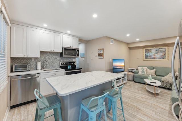 kitchen featuring light stone countertops, appliances with stainless steel finishes, white cabinetry, sink, and a breakfast bar area