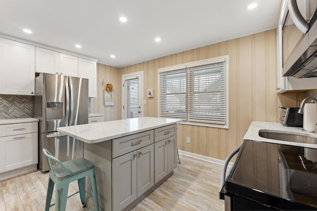 kitchen featuring white cabinets, appliances with stainless steel finishes, a kitchen bar, gray cabinets, and light stone counters