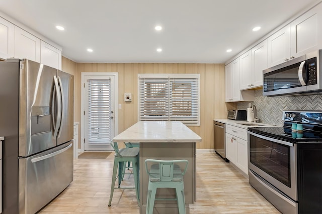 kitchen with white cabinets, stainless steel appliances, a center island, and light stone counters