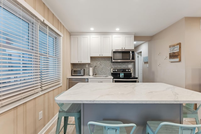 kitchen with sink, white cabinetry, light stone countertops, a breakfast bar, and stainless steel appliances