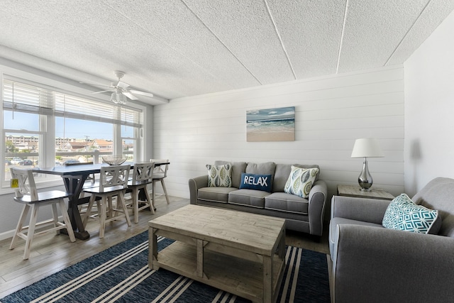 living room with hardwood / wood-style flooring, ceiling fan, a textured ceiling, and wood walls