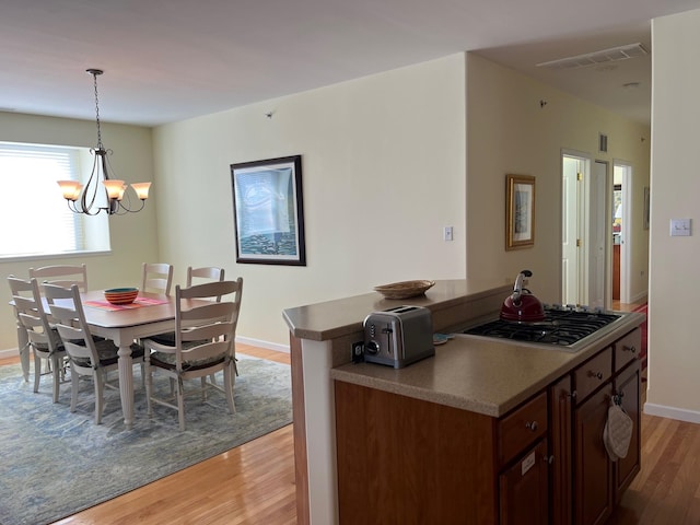 kitchen with stainless steel gas stovetop, light wood-type flooring, pendant lighting, and a notable chandelier