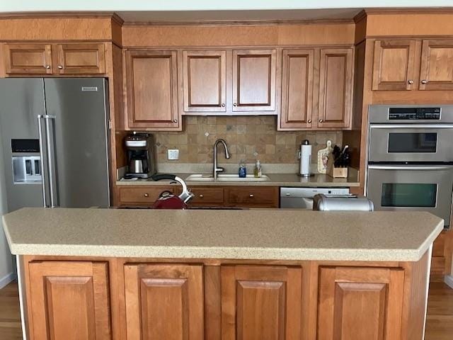 kitchen with stainless steel appliances, sink, hardwood / wood-style floors, decorative backsplash, and a center island with sink