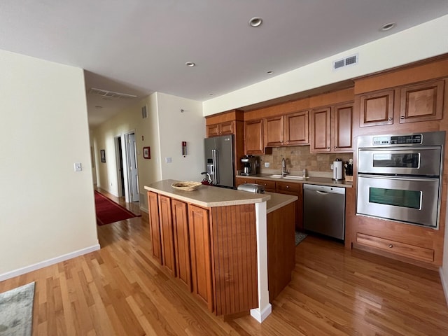 kitchen featuring light hardwood / wood-style flooring, a center island, stainless steel appliances, decorative backsplash, and sink