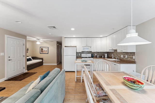 kitchen featuring white appliances, white cabinets, sink, hanging light fixtures, and light wood-type flooring