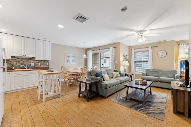 living room with light wood-type flooring, ceiling fan, and sink