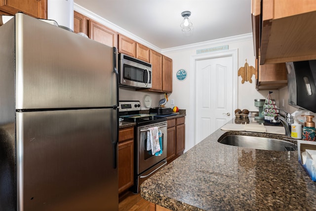 kitchen featuring sink, stainless steel appliances, dark stone countertops, crown molding, and hardwood / wood-style floors