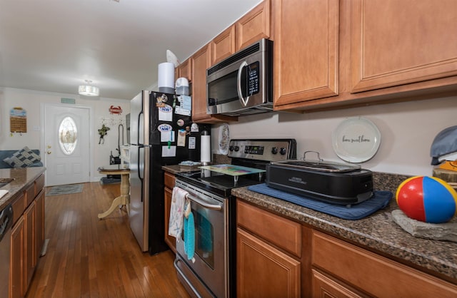 kitchen featuring dark hardwood / wood-style flooring, dark stone countertops, crown molding, and appliances with stainless steel finishes