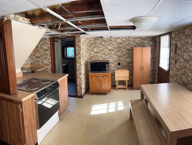 kitchen with electric stove, a sink, a drop ceiling, and brown cabinetry