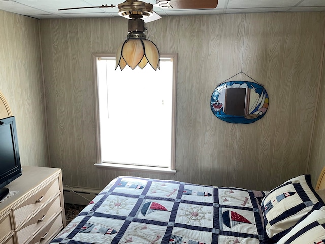 bedroom featuring a baseboard radiator, wooden walls, and a paneled ceiling