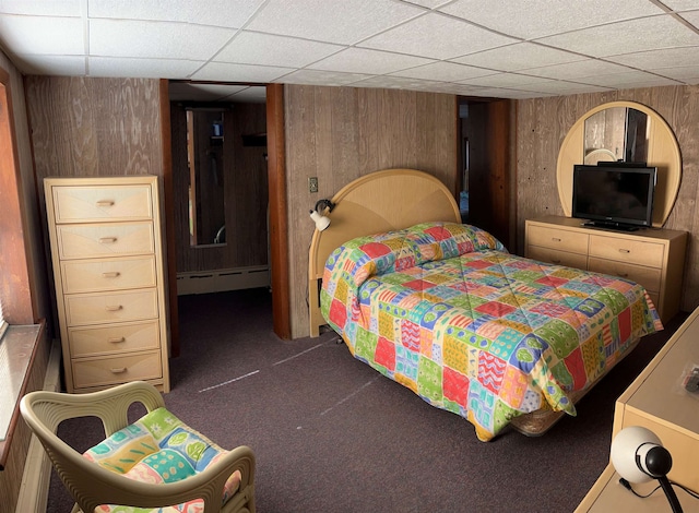 bedroom with carpet flooring, wood walls, a drop ceiling, and baseboard heating