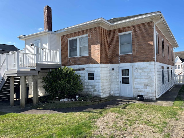 back of house featuring a chimney, stairs, a wooden deck, brick siding, and a lawn