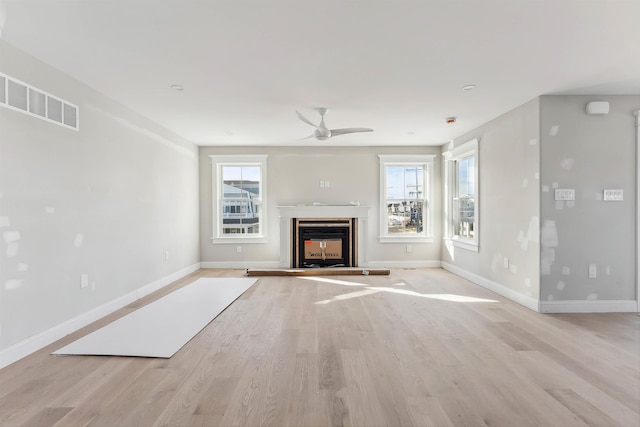 unfurnished living room with a multi sided fireplace, plenty of natural light, and light wood-type flooring