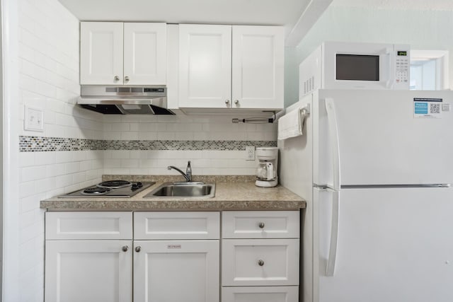 kitchen with white appliances, under cabinet range hood, a sink, white cabinetry, and backsplash