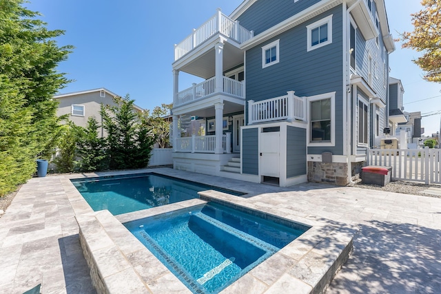 rear view of property with an in-ground hot tub, fence, a balcony, and a patio area