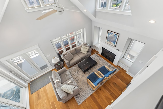 living room featuring a towering ceiling, wood finished floors, a glass covered fireplace, a ceiling fan, and recessed lighting