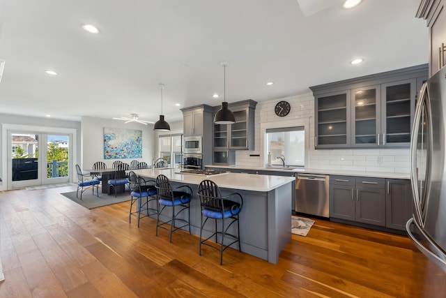 kitchen with appliances with stainless steel finishes, gray cabinetry, a center island with sink, a kitchen breakfast bar, and recessed lighting
