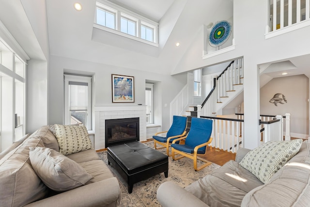 living area with high vaulted ceiling, recessed lighting, wood finished floors, a brick fireplace, and stairs